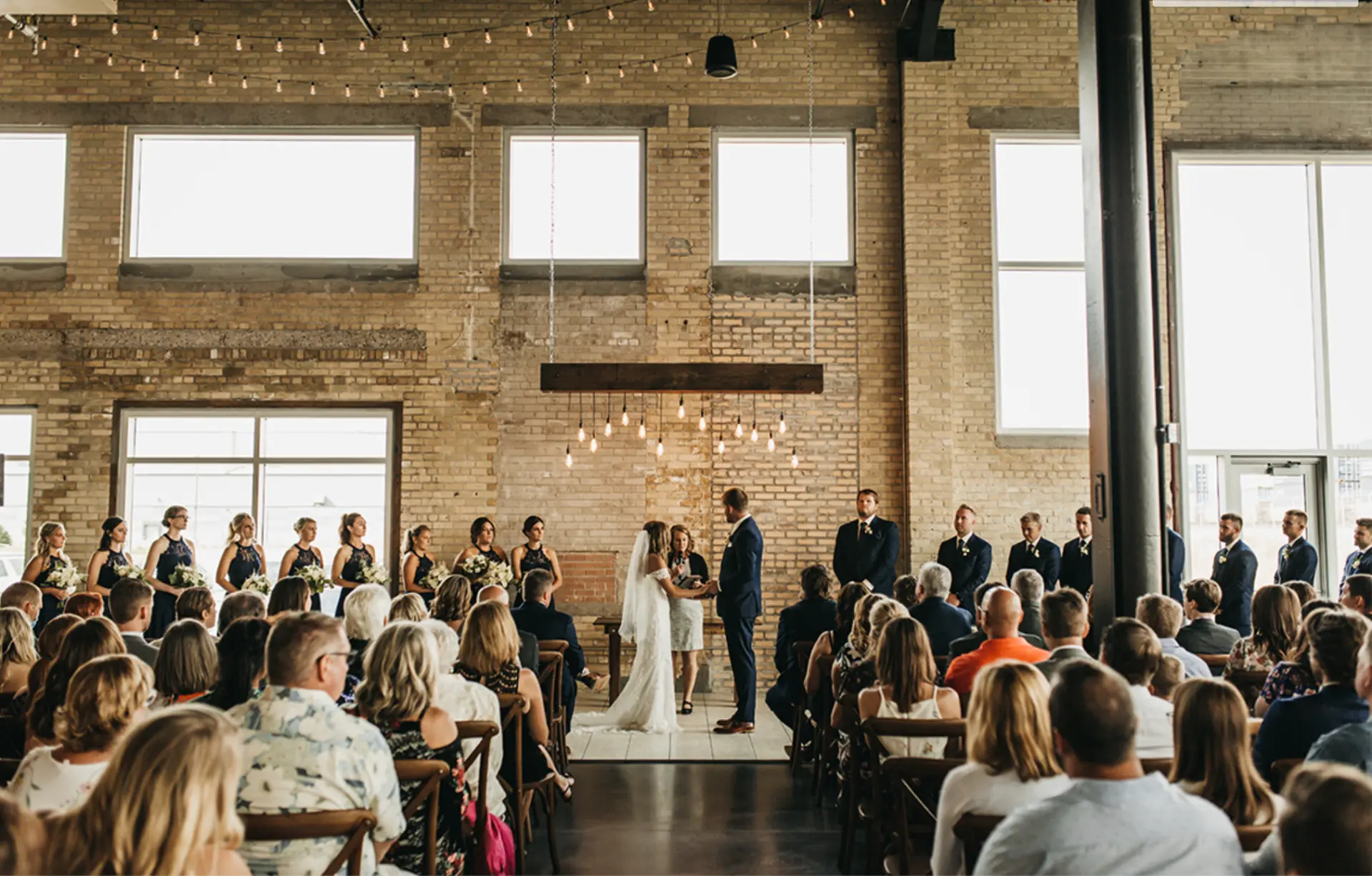A wedding ceremony in the event hall with brick walls and string lights